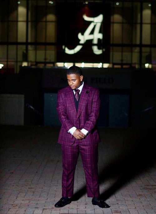 Burgundy houndstooth plaid suit with a fitted silhouette. Wide peak lapels, two-button jacket, and tailored trousers. Includes a vest, matching tie, and black shoes. Classic men's formal wear.