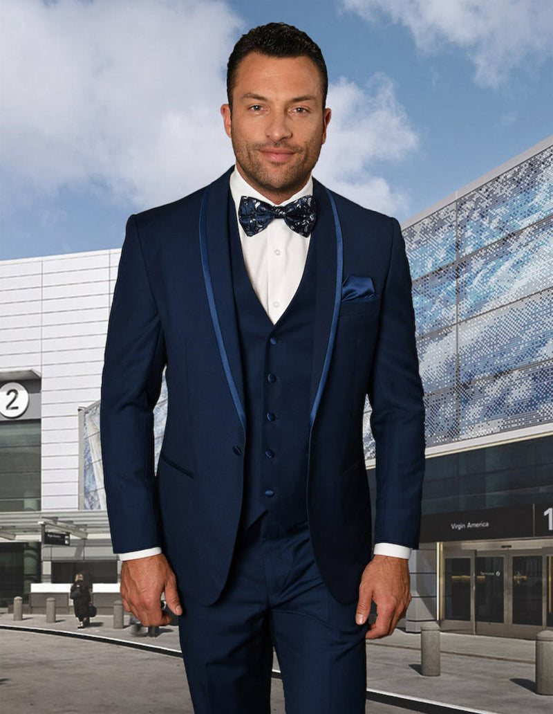 Men's sapphire blue tuxedo with shawl lapel and satin trim. Tailored fit, six-button vest, and matching bow tie. Crafted from smooth, subtly sheened fabric.