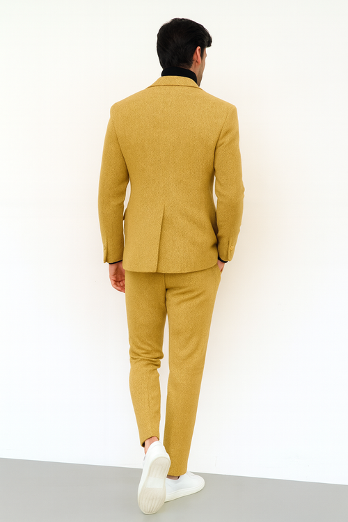 Men's gold double-breasted suit with herringbone texture, two-button closure, and notched collar. Tailored trousers match. Worn with white sneakers for a modern look.