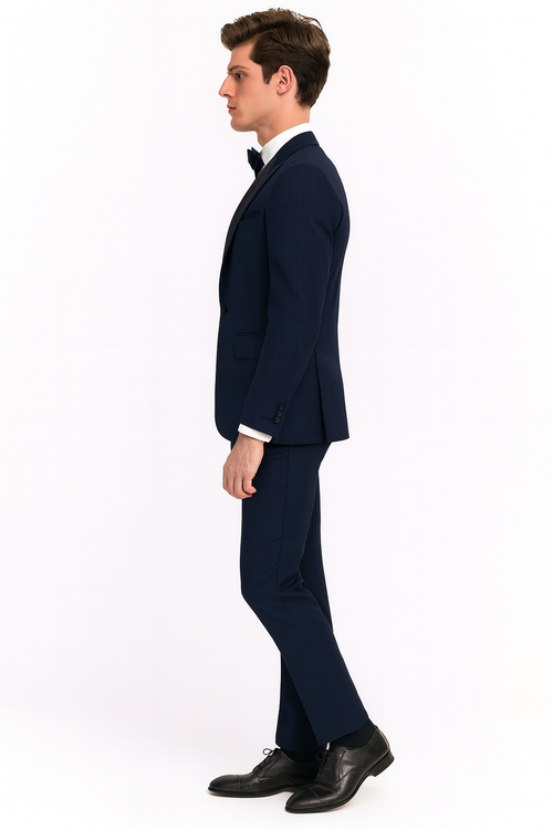 Navy blue men's tuxedo with satin peak lapel and matching sateen details. Includes fitted blazer and tailored trousers. Styled with white shirt, black bow tie, and dress shoes. Subtle patterned fine weave fabric.