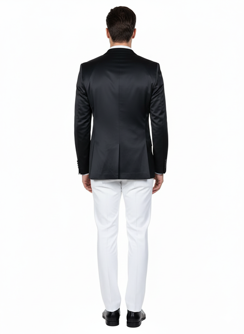 Black satin men's blazer. Slim fit, two-button closure, single vent. Shiny black satin. Worn with white trousers. Structured shoulders, long sleeves, refined formal silhouette.