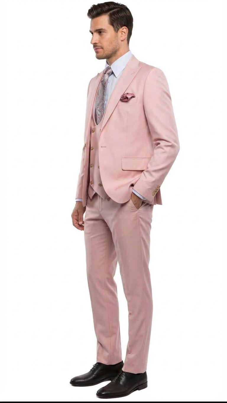 Men's blush pink three-piece suit: fitted blazer, vest, tailored trousers. Gold buttons, soft pink fabric. Styled with a light blue shirt, patterned tie, pocket square.