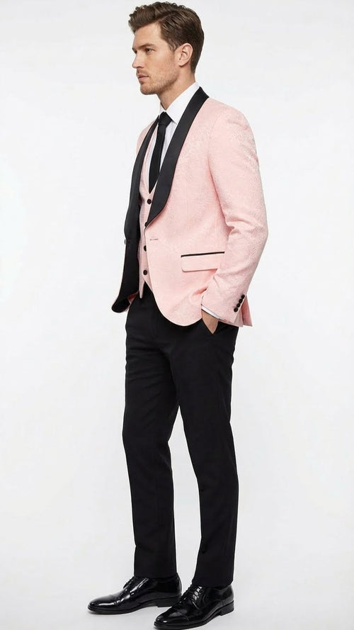 Blush pink tuxedo suit for men: Blazer w/ black shawl lapel & trim. Matching pink vest, slim-fit black trousers, and black tie. Tailored silhouette.