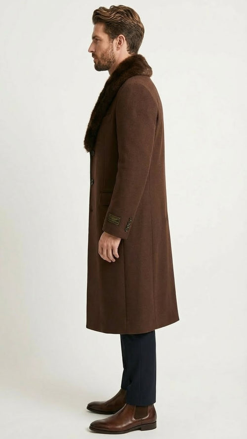 Men's brown long overcoat with faux fur collar, textured fabric, and knee-length straight silhouette. Features three buttons, side pockets, and buttoned sleeves. Paired with dark trousers and brown leather boots.