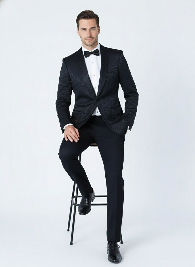 Alberto Nardoni men's black tuxedo suit. Features textured paisley floral pattern. Includes structured jacket with single-button closure, peaked lapels, and matching tailored trousers. Paired with a white shirt and black bow tie.