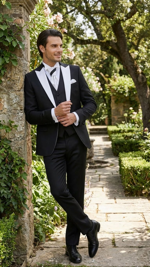 Men's black & white prom tuxedo: black jacket with white satin lapel, black vest, slim-fit black trousers. Includes white shirt & patterned tie. Structured, formal design.