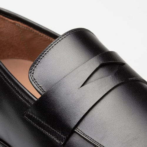 Black leather Mezlan Avenue penny loafer. Sleek, slip-on style with a rounded toe and decorative vamp strap. Tan interior lining contrasts the black exterior. Visible stitching details.