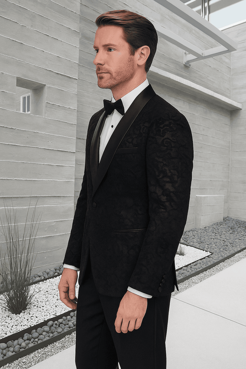 Men's black paisley velvet double-breasted tuxedo jacket. Shawl collar, pocket, and button cuffs. Formal cut, structured shoulders. Paired with white vest and black trousers.