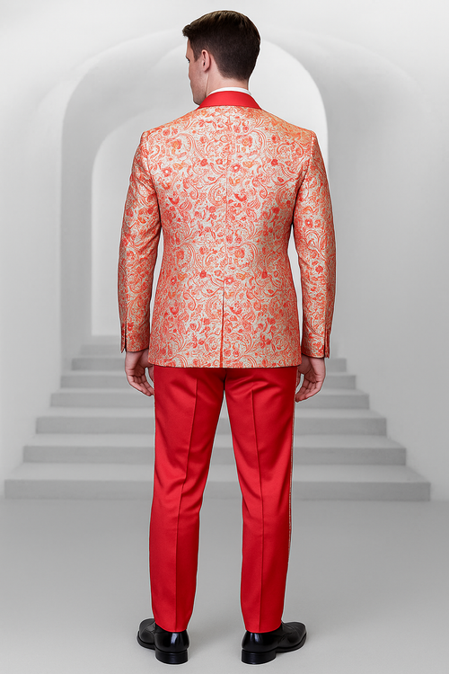 Coral orange men's shiny paisley wedding tuxedo. Intricate paisley patterns on the jacket with structured silhouette, back vent. Red trousers and solid red collar. Smooth, glossy materials for a formal design.