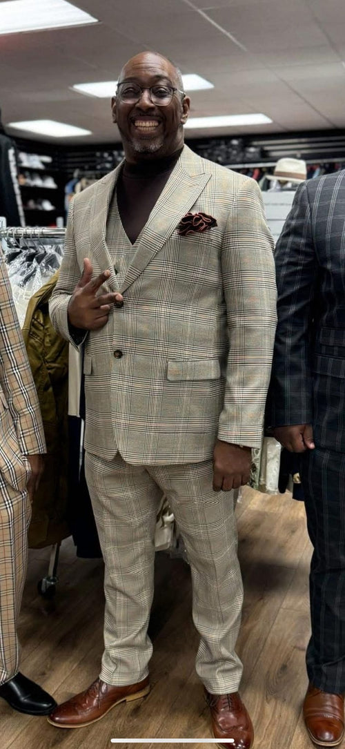 Men's beige plaid 3-piece suit. Fitted blazer with notch lapel, two buttons, and chest pocket. Matching trousers and a three-button waistcoat. Textured fabric with light/dark beige checks. Worn with brown leather shoes.