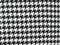 Black houndstooth hybrid double-breasted jacket. Structured, tailored fit with repeating black and white pattern. Textured fabric, potentially outerwear material. Formal style, double-breasted buttons.