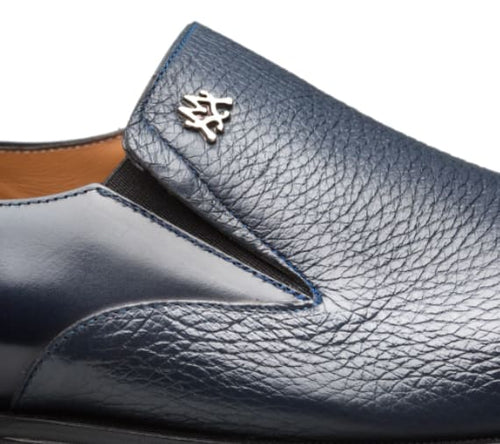 Blue calfskin slip-on shoe with a v-shaped opening. Textured exterior, metallic emblem detail. Tan interior lining for comfort.