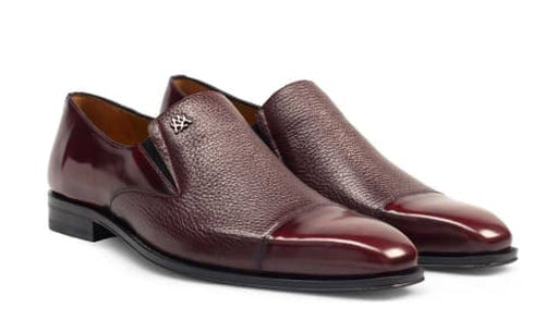 Milani burgundy slip-ons crafted from calfskin and deerskin feature a pointed toe, textured panel, and low heel. Sleek silhouette with a small emblem, designed for formal wear.
