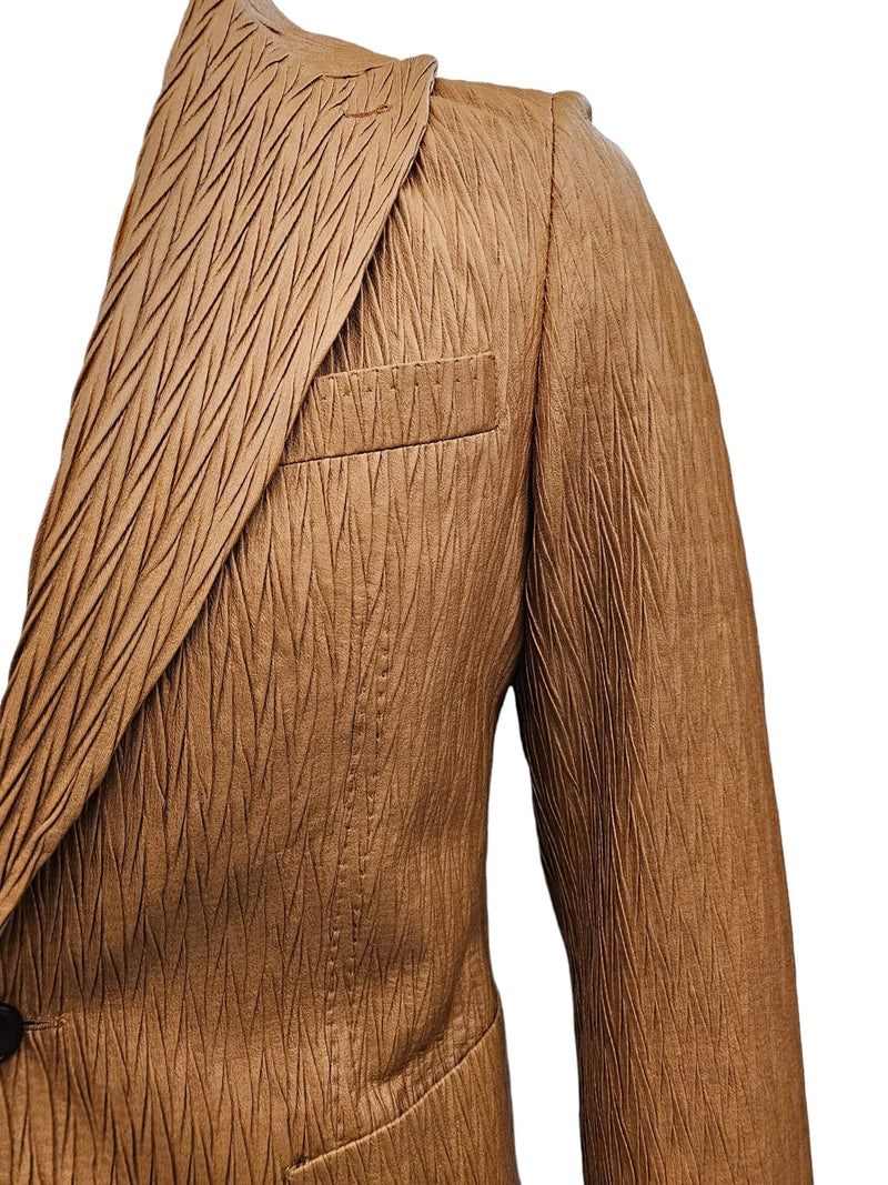 Tan vegan leather men's suit. One-button, peak lapel design with textured, elongated diamond pattern. Fitted shoulder and sleeve. Visible left pocket.