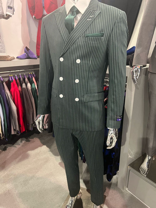 Green pinstripe double-breasted suit. Fitted jacket w/ notched lapel, silver buttons. Vertical white stripes. Slim-fit trousers. Green pocket square & tie complete the look.