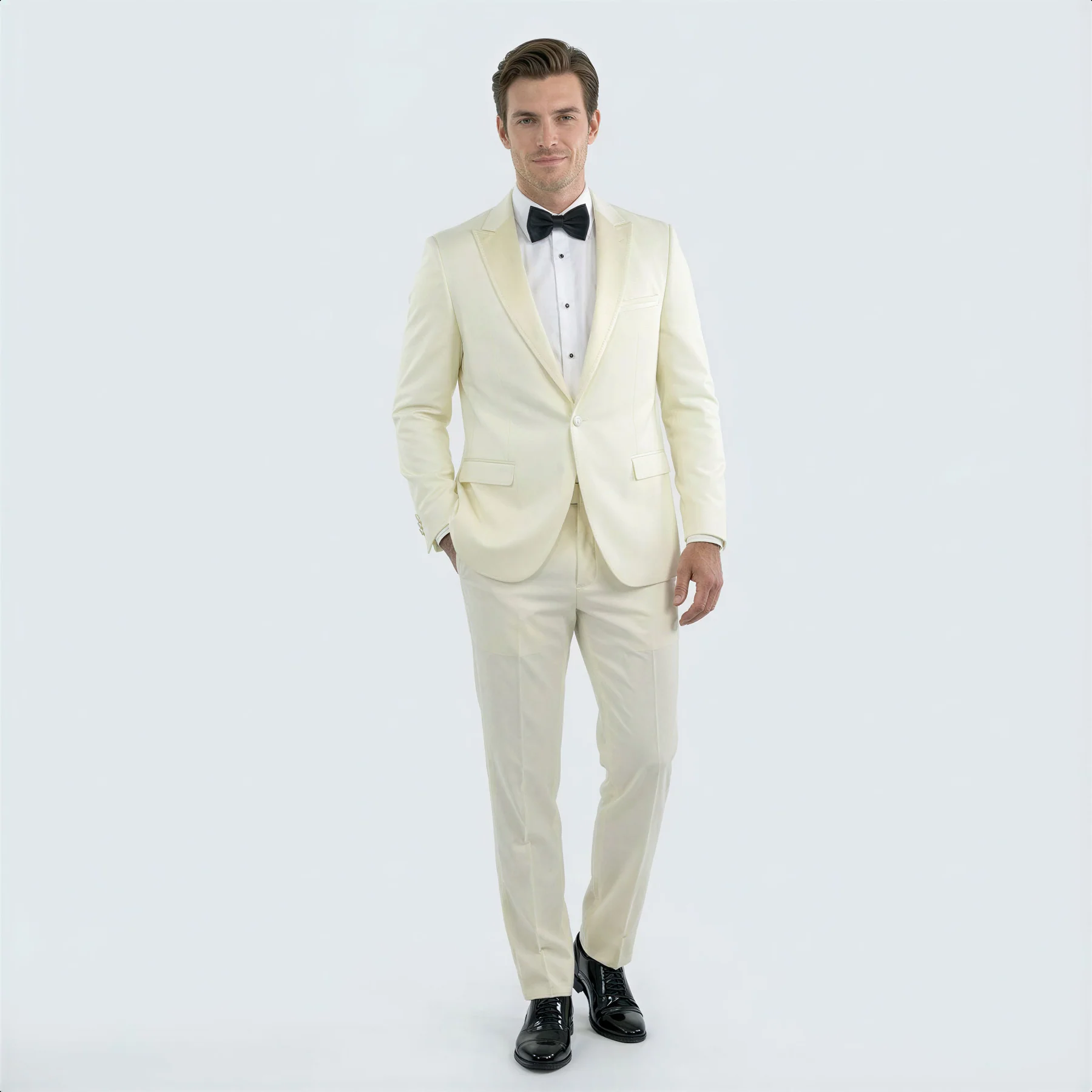 Ivory peak lapel slim fit tuxedo. Single-breasted jacket with notch lapels, matching trousers. Smooth ivory fabric. Includes front pockets. Styled with black bow tie, white shirt & shiny black dress shoes.