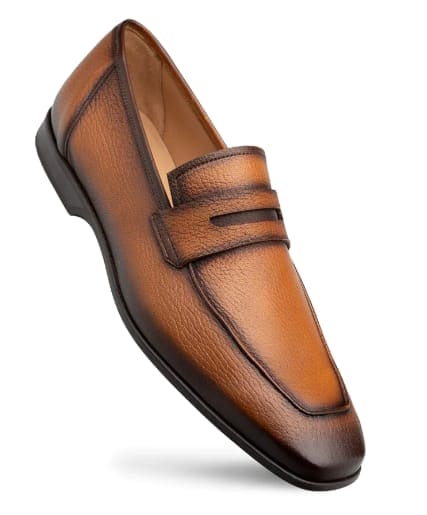 Cognac deerskin penny loafers with a streamlined silhouette. Rounded toe, low heel, and textured cognac leather upper. Features dual stitched accents. Flat black sole. Simple, classic design.