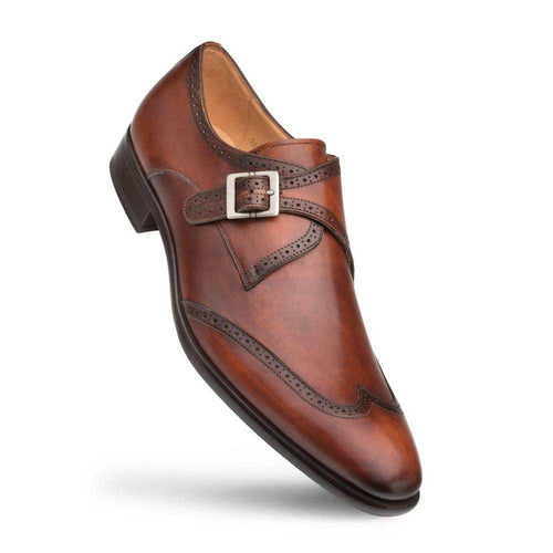Cognac calfskin Mezlan monk strap with polished finish, wingtip details, and metal buckle closure. Features a rounded toe, contrasting dark sole, and decorative perforations.