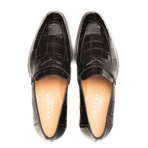 Mezlan Piccolo black alligator penny loafer. Sleek, elongated shape, low heel. Textured black alligator upper with crocodile pattern. Tan lined interior with branding. Classic penny strap.