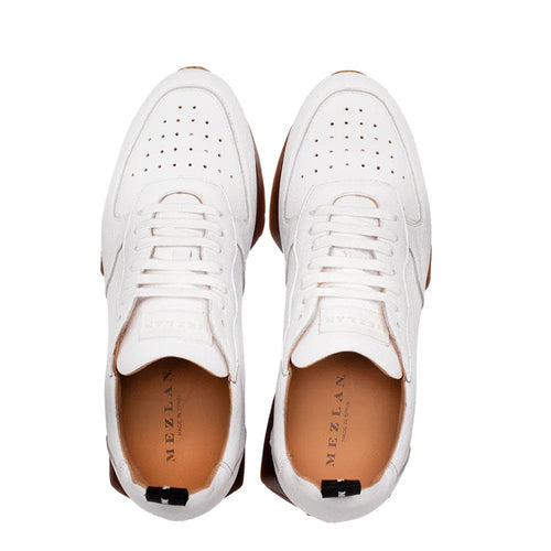Mezlan Gerardo white deerskin sneakers with perforated sides, white lace-up, and brown rubber sole. Tan leather lining and a black back tab complete the design.