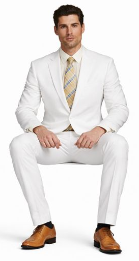 White, tailored suit with a single-breasted jacket and matching trousers. Lightweight, smooth material. Paired with a light dress shirt and yellow/blue striped tie. Light brown, lace-up leather shoes.