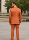 Luxury men's orange pinstripe suit: tailored jacket (single vent, peak lapels, button sleeves) & slim-fit trousers. Bold, saturated color, textured fabric with lighter pinstripes. Elegant, formal silhouette.