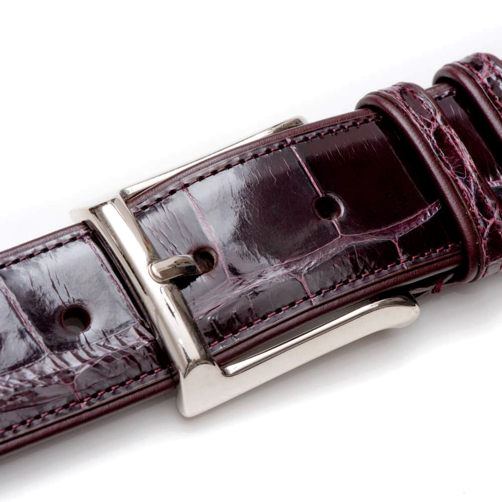 Burgundy Mezlan AO7907 alligator belt. Glossy, textured leather. Silver-toned buckle. Adjustable fit. Luxurious alligator skin construction.