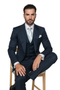 Navy wool suit with classic fit: single-breasted jacket, vest, pleated wide-leg trousers. Smooth texture, well-tailored. Features pocket square and light tie.