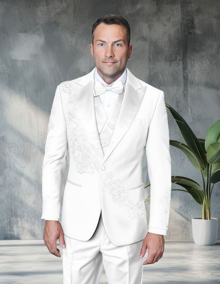 Modern fit three-piece tuxedo in white, featuring floral appliqué on the left side of the jacket. The tuxedo includes a satin shawl lapel and a three-button closure. A matching vest is worn underneath the jacket, complemented by a bow tie.