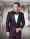 The Statement men's 2-piece modern fit tuxedo features a burgundy fabric with a textured pattern and floral appliqué detailing on the lapels and front. It has a black satin shawl collar and is paired with a classic white dress shirt and black bow tie.