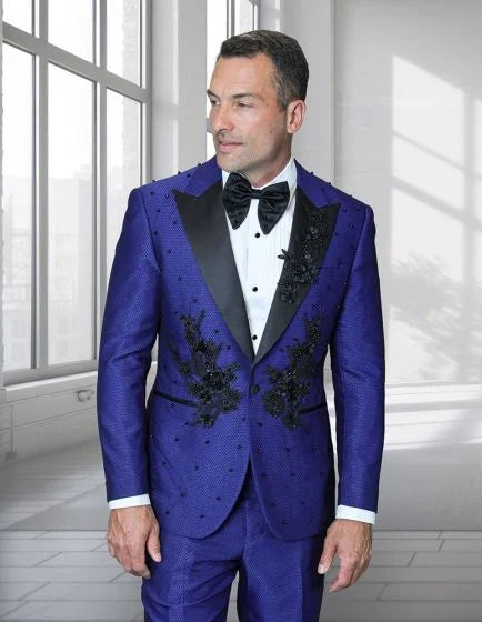 Statement men's 2-piece modern fit tuxedo features a fitted jacket and matching trousers. The jacket is primarily a vibrant purple with a textured finish, black satin lapels, and intricate floral appliqué detailing on the front. The ensemble includes a white dress shirt and a black bow tie.