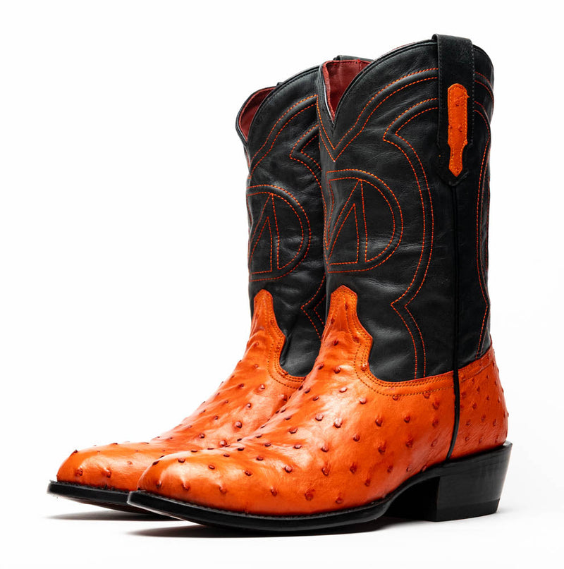 Marco Di Milano cowboy boots in orange ostrich leather with a round toe and black accents. Featuring decorative stitching, pull tabs, and a classic cowboy boot shape. Solid black heel.