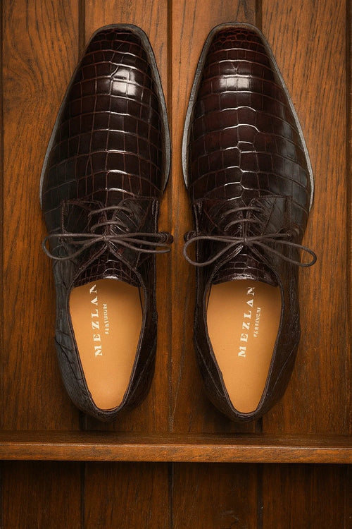 Men's brown alligator derby shoes. Genuine alligator skin with a polished, textured finish. Elongated shape, lace-up closure, and sleek profile. Rich brown color.