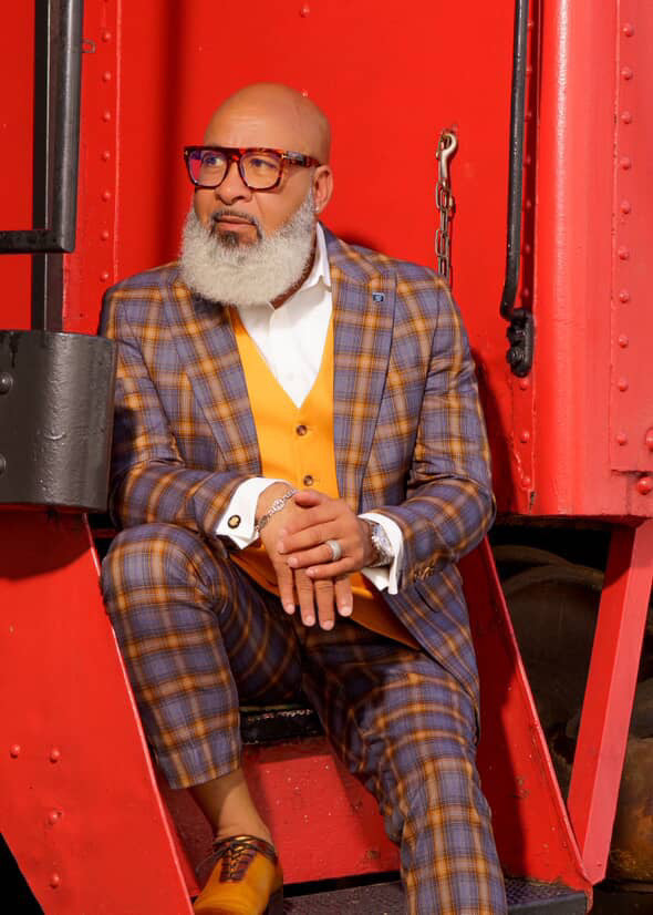 Men's Stacy Adams suit: grey/gold plaid jacket & slim-fit pants. Includes orange vest, white dress shirt, and a watch. Bold windowpane pattern.
