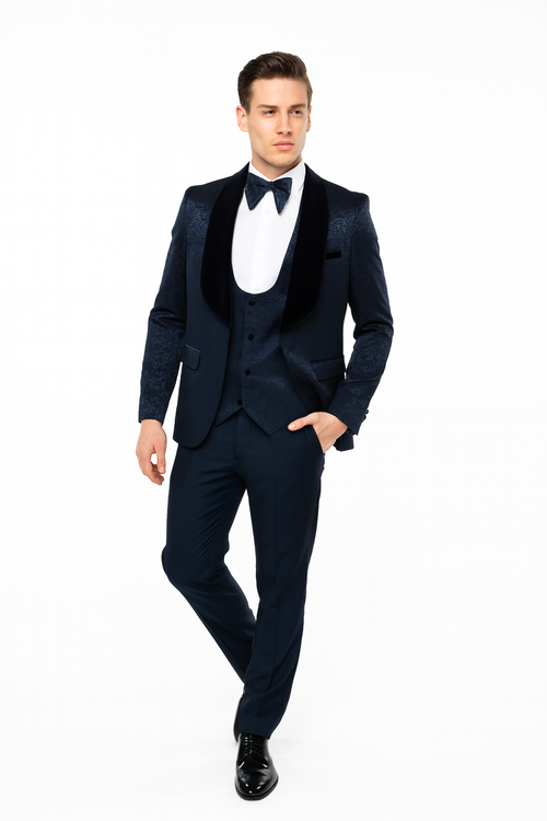 Navy jacquard tuxedo with black velvet shawl lapel. Tailored jacket, structured shoulders, fitted waist. Flat-front trousers. White shirt and bow tie complete the formal look.
