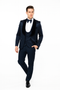 Navy jacquard tuxedo with black velvet shawl lapel. Tailored jacket, structured shoulders, fitted waist. Flat-front trousers. White shirt and bow tie complete the formal look.
