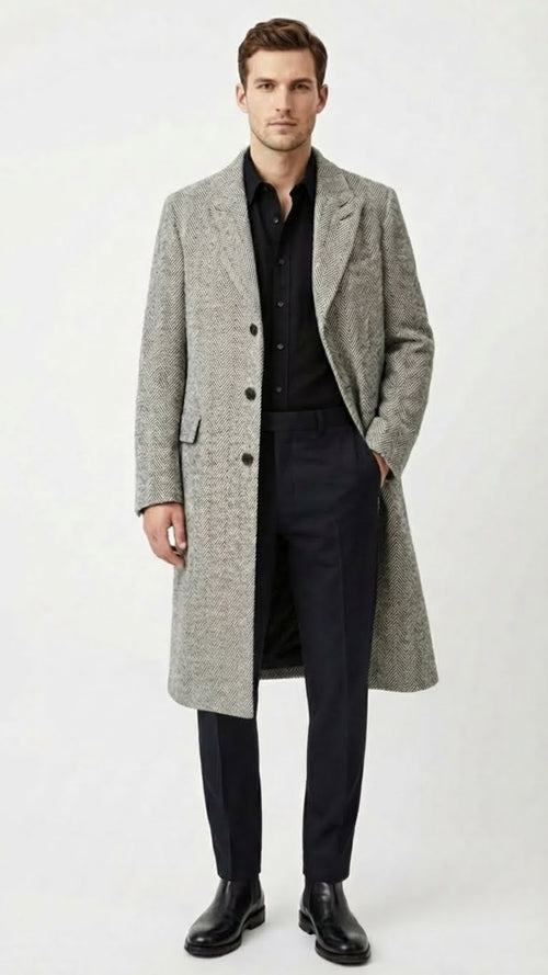 Alberto Nardoni men's grey herringbone overcoat: tailored silhouette, mid-length, structured shoulders, single-breasted. Features herringbone pattern, side pockets, back vent. Formal look, paired with dark trousers and boots.
