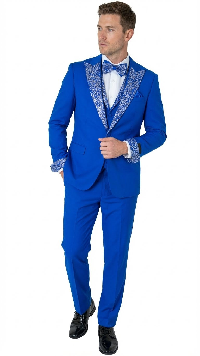 Royal blue tuxedo suit with white embellished lapel, matching bow tie, and sleeve details. Pleated blue trousers complete the structured, vibrant look.
