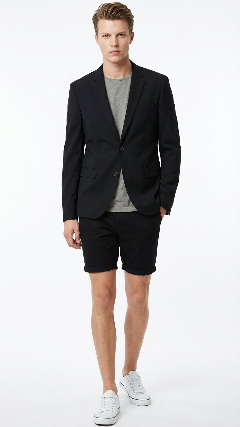 Men’s black summer business suit features a fitted black blazer with two buttons and notched lapels, paired with matching black shorts. The blazer has two front pockets and structured shoulders, while the shorts are knee-length with a cuffed hem. A gray t-shirt is worn underneath the blazer.