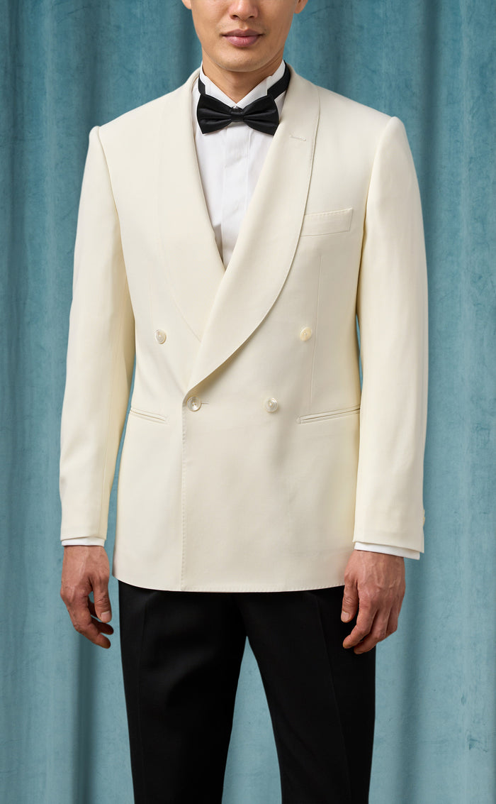 Ivory double-breasted men's dinner jacket. Cream color, smooth fabric, notched lapels, two buttons. Slim pockets, paired with black trousers.

