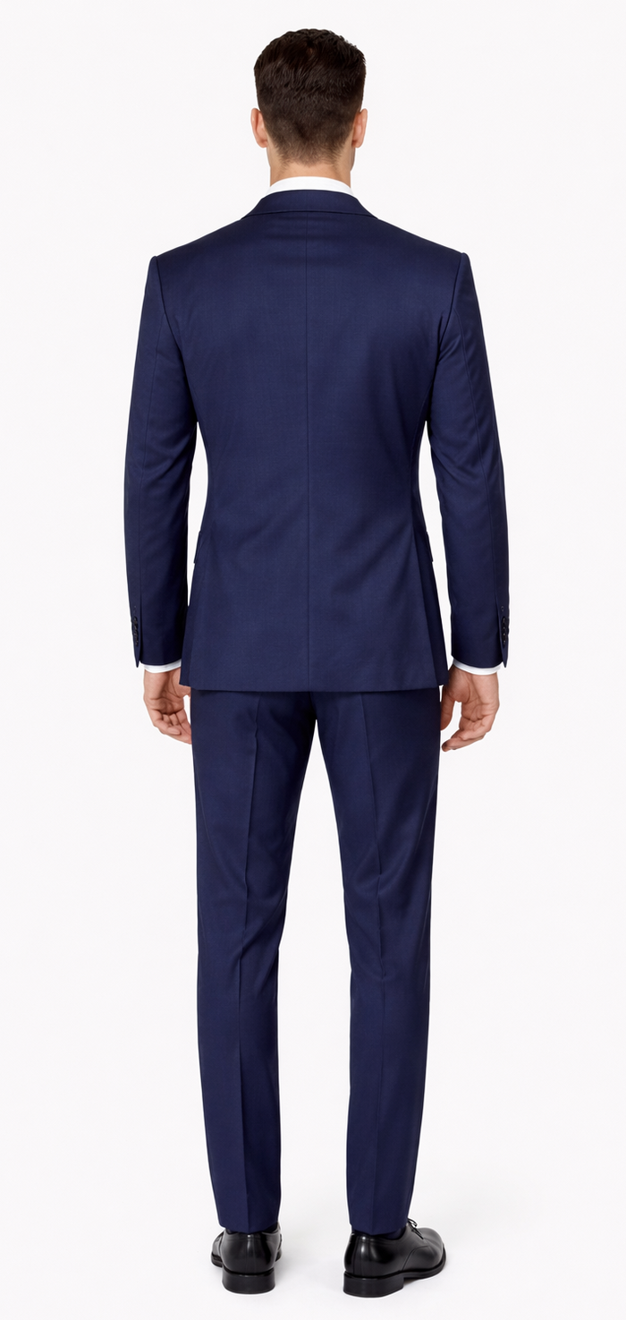 Navy blue tuxedo: peak lapel, fitted, structured shoulders, textured fabric. Straight-cut pants. Back view. Smooth silhouette. Matching color jacket and pants.

