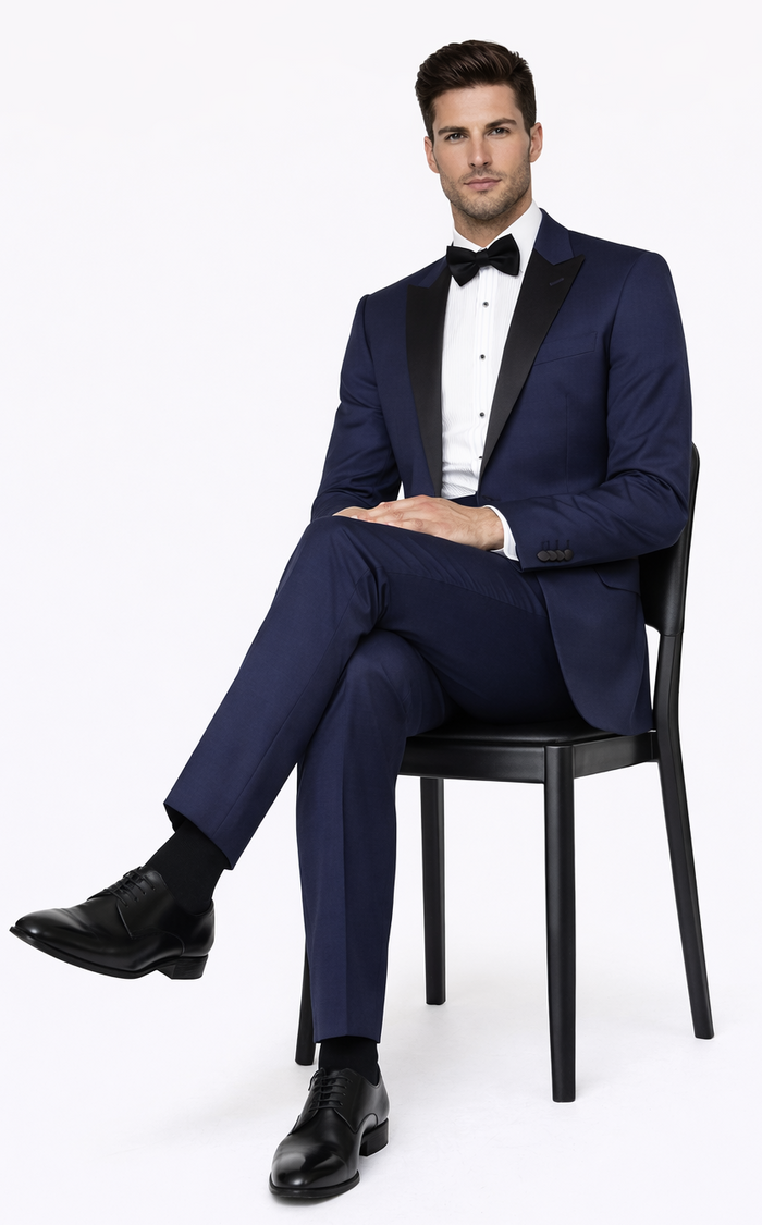 Navy blue Great Gatsby tuxedo with peak lapels & black satin contrast. Single-breasted, tailored fit. Paired with white shirt, bow tie, straight-cut trousers & black leather shoes.
