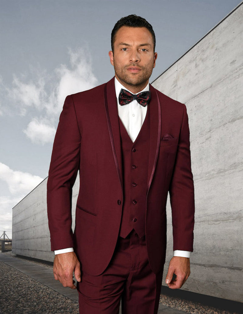 Burgundy men's tuxedo with vest, shawl lapels, and satin trim. Tailored fit with a structured silhouette. Includes matching trousers, button-up front, and side pockets. Smooth fabric.
