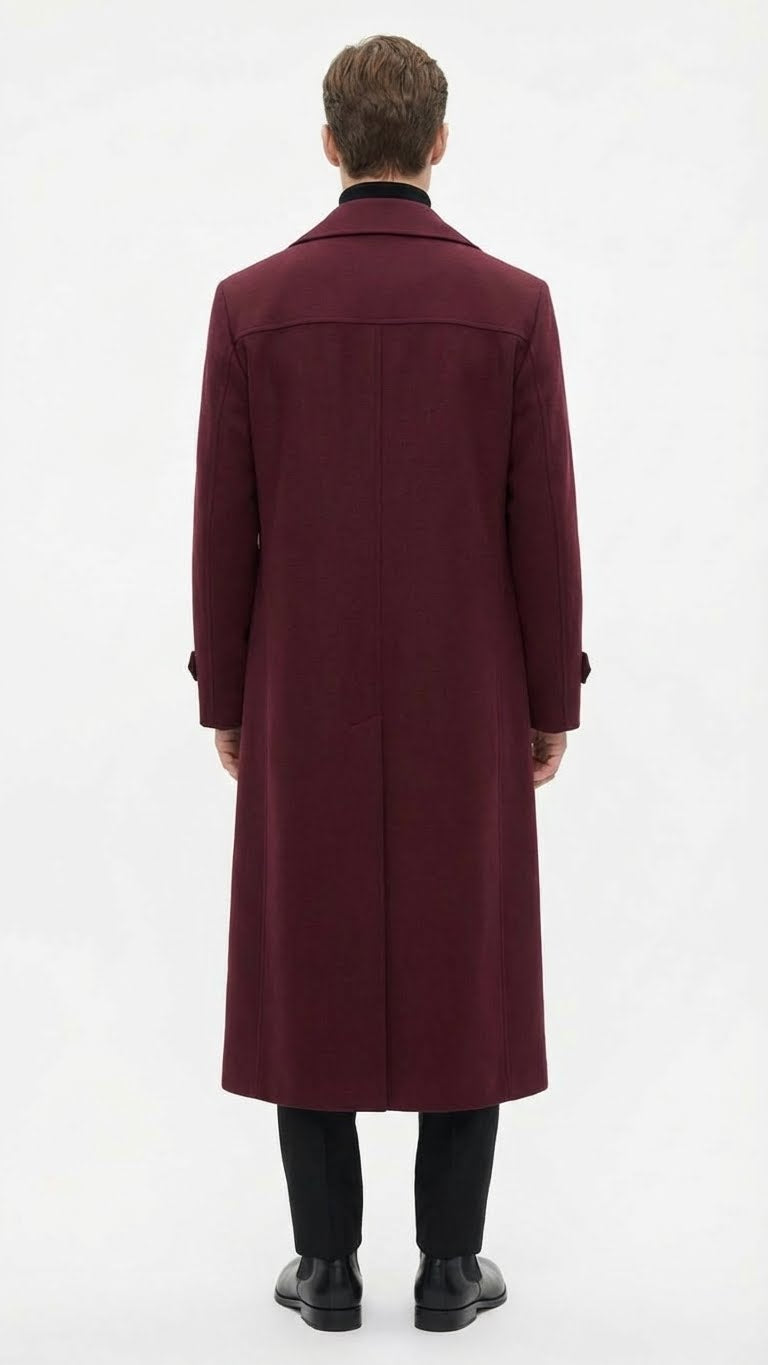 Burgundy men's full-length overcoat. Straight cut, tailored fit, notched collar, long sleeves. Solid fabric. Back: vertical seam, slight hem flare. Worn with black trousers and shoes.
