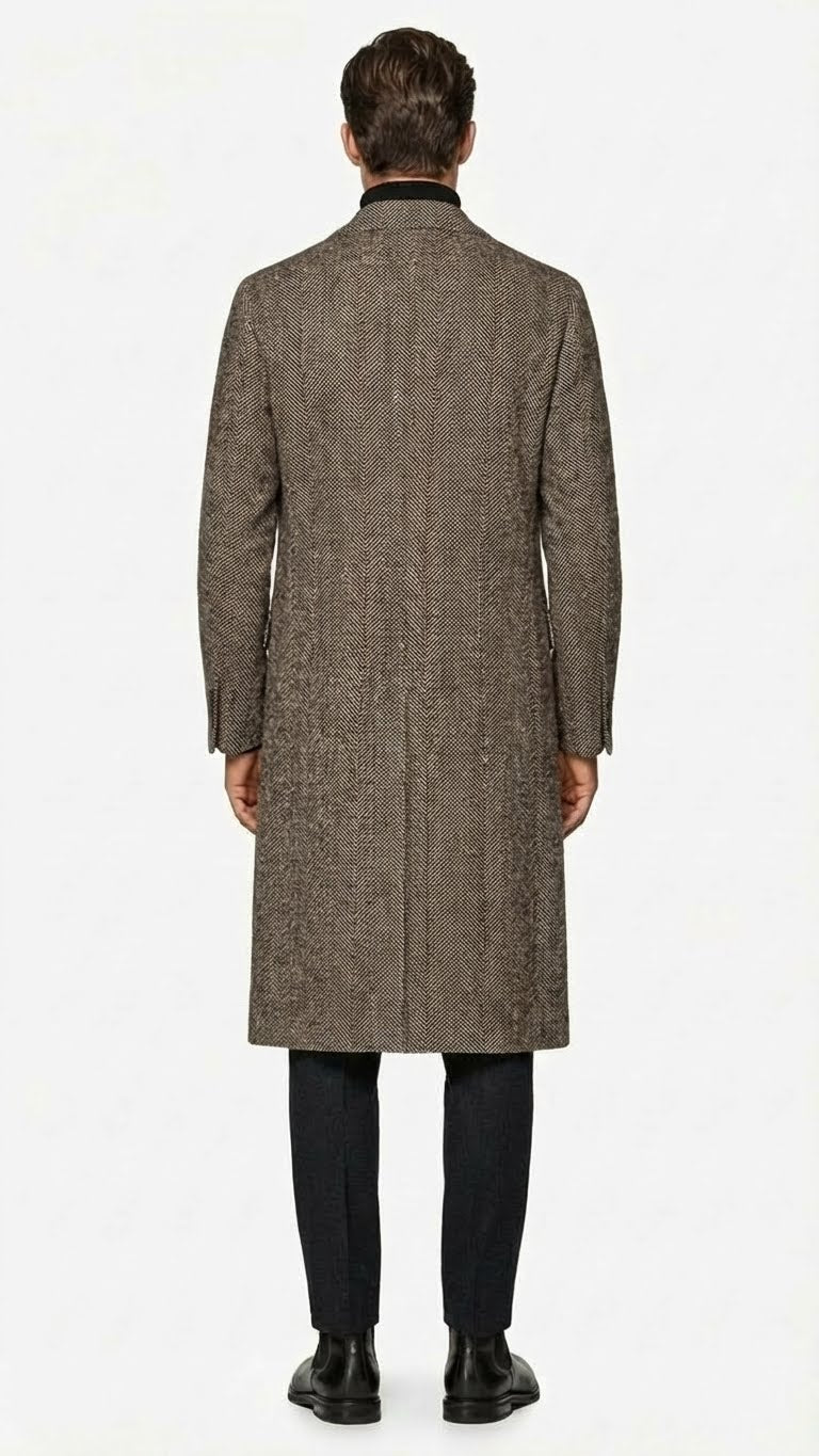 Men's black & grey herringbone tweed overcoat. Long, straight, single-breasted wool blend. Notched collar, side vents, & visible stitching. Structured, textured design.
