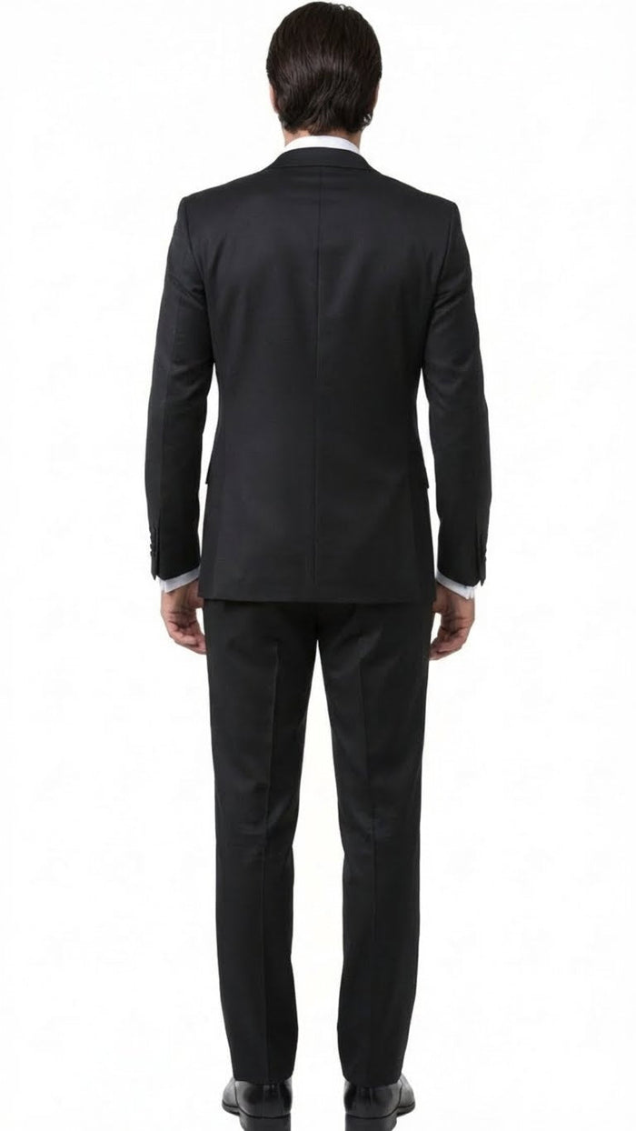 Black men's tuxedo suit viewed from the back. Fitted silhouette, structured design, smooth black fabric. Single vent jacket, matching trousers, and black shoes complete the formal look.
