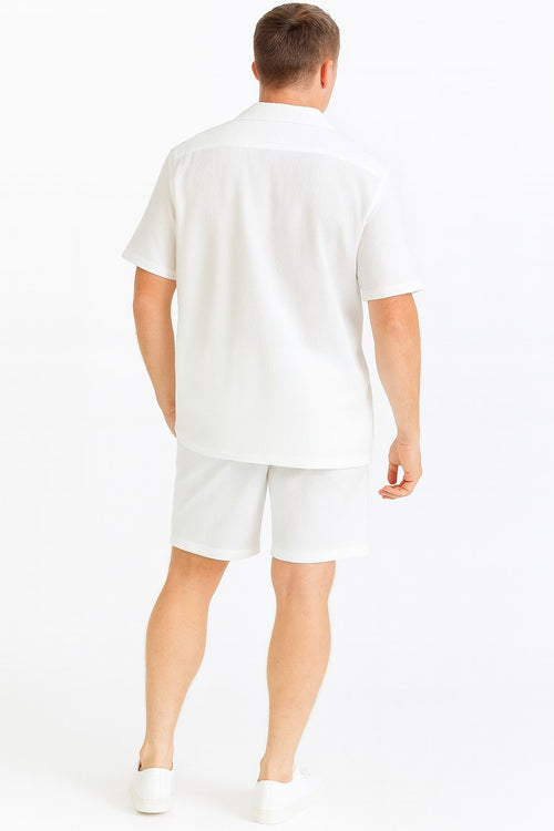 Men's white seersucker short set: short-sleeved button-up shirt and matching shorts in lightweight, textured fabric. Relaxed fit, shirt slightly longer. Shorts: straight cut, above the knee. Uniform color and design.
