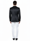 Black satin men's blazer. Slim fit, two-button closure, single vent. Shiny black satin. Worn with white trousers. Structured shoulders, long sleeves, refined formal silhouette.
