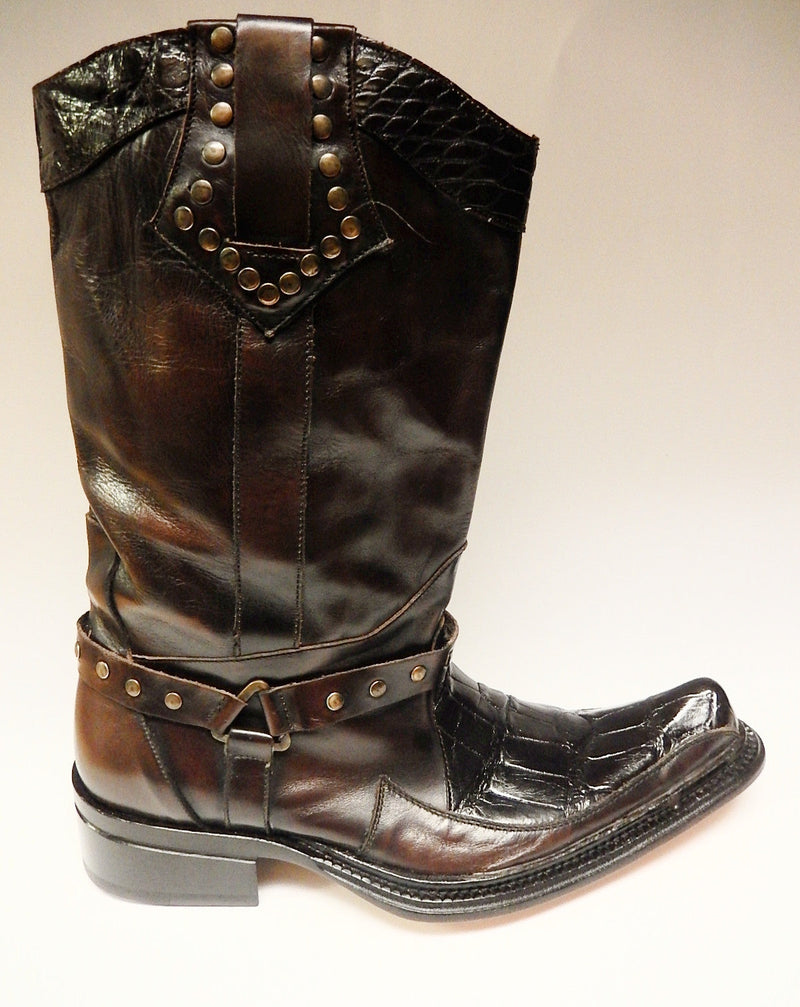 Mauri alligator calf knee boots, style 44238. Tall, brown leather boots with a black alligator pattern on the upper shaft. Decorated with metal studs and a strap. Pointed toe, textured sole, and a slight heel.
