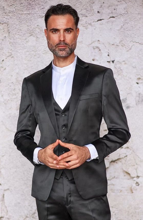 Men's slim-fit, three-piece suit crafted from shiny black satin. Features a jacket (notched lapel, chest pocket), matching three-button vest, and trousers. Worn over a white shirt.
